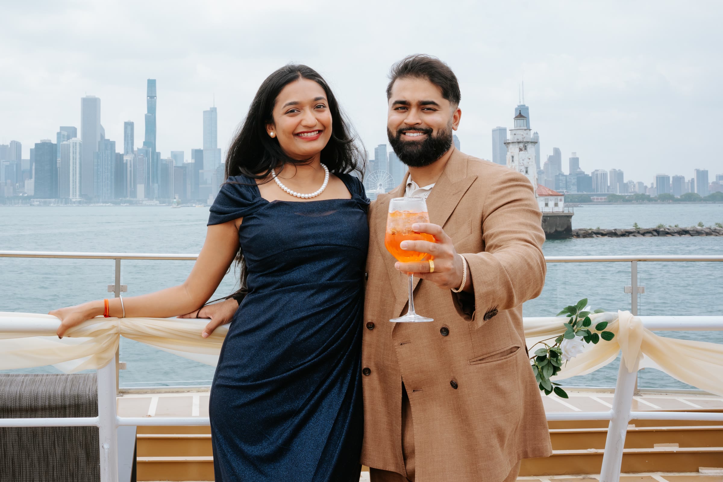 Nish and Pooja on a boat, a city skyline behind them