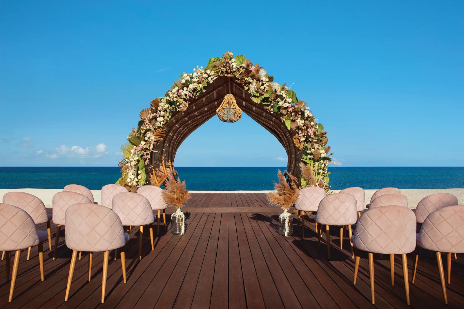 A flower-covered wedding arch on a wooden deck at Dreams Natura, the sea behind it